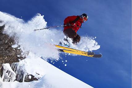 Bei der Abfahrt auf einer Piste springt ein Skifahrer von einem kleinen Felsen.