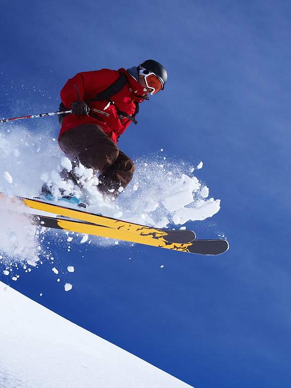 Bei der Abfahrt auf einer Piste springt ein Skifahrer von einem kleinen Felsen.