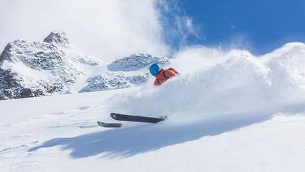 Bei der Abfahrt auf einer Piste springt ein Skifahrer von einem kleinen Felsen.