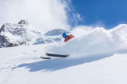 Bei der Abfahrt auf einer Piste springt ein Skifahrer von einem kleinen Felsen.