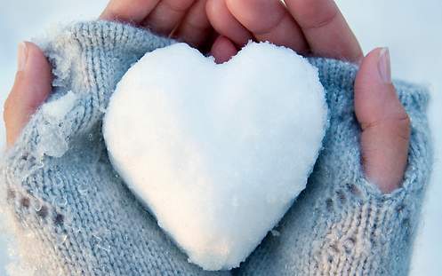 Zwei Hände halten ein aus Schnee geformtes Herz.