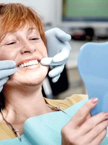 Eine ältere Dame bekommt beim Zahnarzt eine Zahnprothese eingesetzt und schaut in den Spiegel.