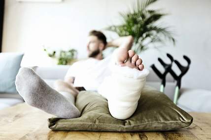 Ein Mann sitzt mit gebrochenem Fuß auf einem Sofa