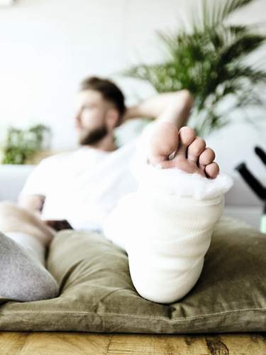 Ein Mann sitzt mit gebrochenem Fuß auf einem Sofa