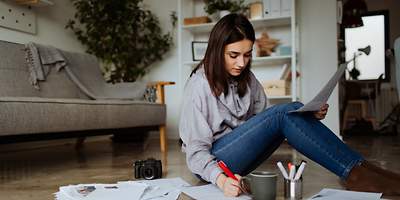 Eine Frau sitzt auf dem Boden und hat viele Blätter um sich herum.