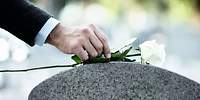 Eine Person legt eine weiße Rose auf einen Grabstein nieder.