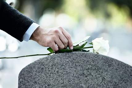 Eine Person legt eine weiße Rose auf einen Grabstein nieder.