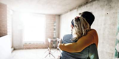 Ein Paar umarmt sich in der Baustelle des Hauses und hat dich wichtigsten Versicherung für den Hausbau abgeschlossen. 
