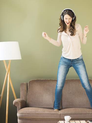 Das Bild zeigt eine junge Frau, die auf einem Sofa tanzt.