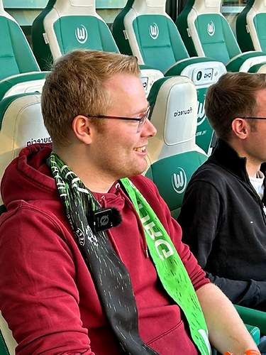 Zwei Männder sitzen auf einer Tribüne im Fußballstadion und freuen sich. 