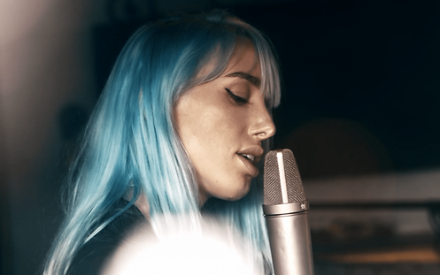 Eine Frau mit blauen Haaren singt in ein Mikrofon