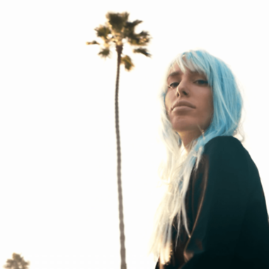 Eine Frau mit hellblauen Haaren schaut in die Kamera