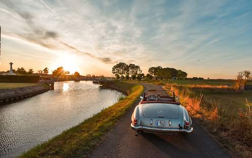 Cabriolet beim Sonnenuntergang neben einem Fluss fahrend