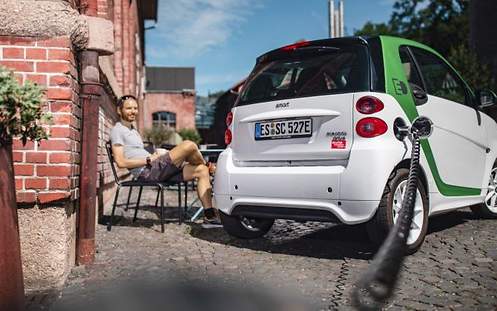 Ein Mann sitzt vor einem Smart Fortwo ED 2013 und läd das Fahrzeug mit Strom auf.