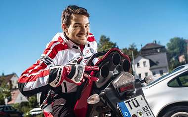 Ein Mann sitzt verkehrt herum auf einem Motorrad und zeigt auf den Auspuff.