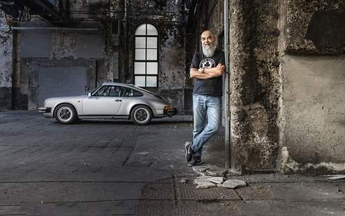 Ein Mann steht in einem alten Gebäude. Neben ihm steht eine Porsche.