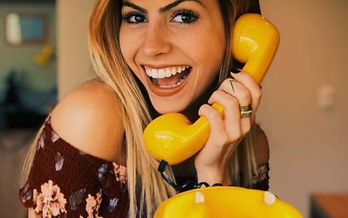 Lachende Frau mit gelbem Telefonhörer in der Hand