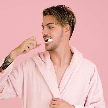 Ein Mann im pinken Bademantel putzt sich seine Zähne