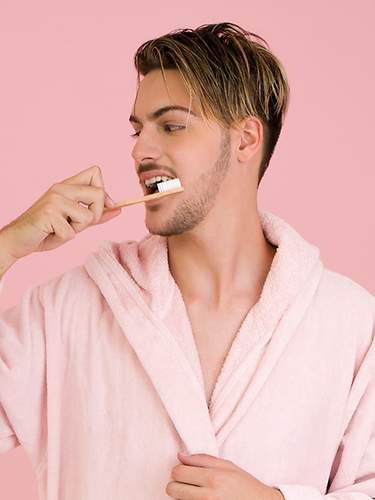 Ein Mann im pinken Bademantel putzt sich seine Zähne