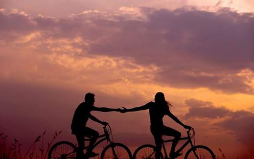 Eine Frau und ein Mann sitzen auf Fahrrädern und berühren ihre Hande.
