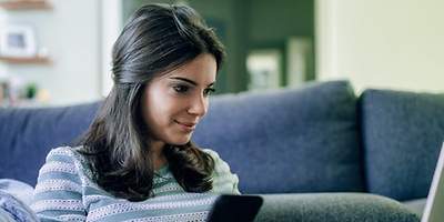 Frau trinkt Kaffee und surft am Handy und am Laptop.