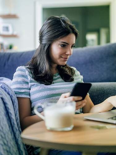 Frau trinkt Kaffee und surft am Handy und am Laptop.