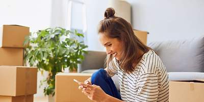 Frau am Handy mit Umzugskartons im Hintergrund