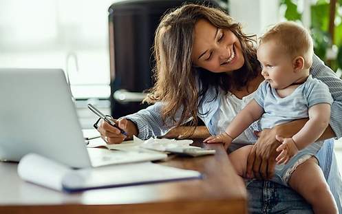 Eine Frau, die im Homeoffice arbeitet und ihr Kind auf dem Arm hat