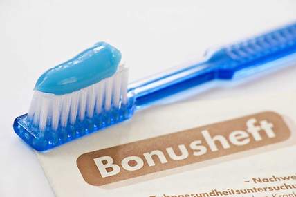 Das Bild zeigt eine Zahnbürste, die auf einem Bonusheft vom Zahnarzt liegt. 