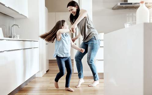 Eine junge Mutter tanzt mit ihrer kleinen Tochter in der Küche.