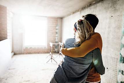 Ein Paar umarmt sich in der Baustelle des Hauses und hat dich wichtigsten Versicherung für den Hausbau abgeschlossen. 