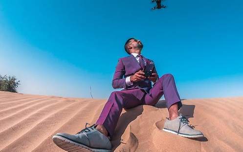 Ein Mann sitzt auf Sand und fliegt eine Drohne